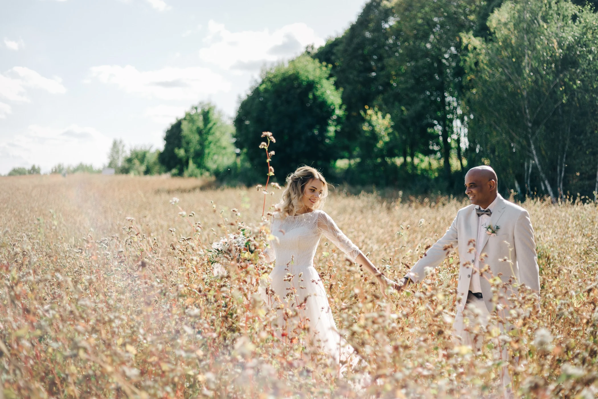 Newlyweds holding hands in a sunlit field